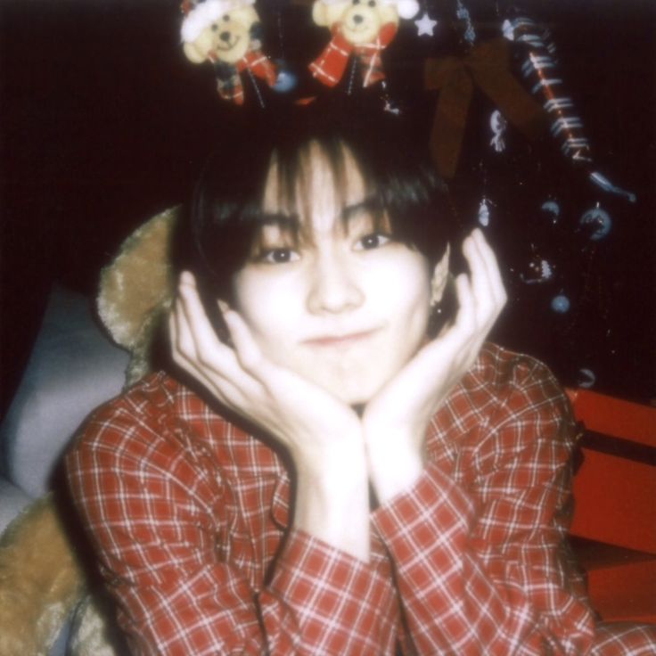 a woman with a teddy bear on her head sitting in front of a christmas tree