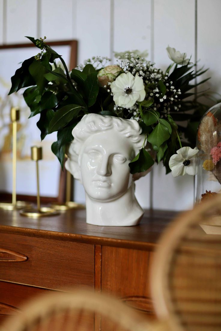 a vase with flowers in it sitting on top of a wooden table next to a mirror