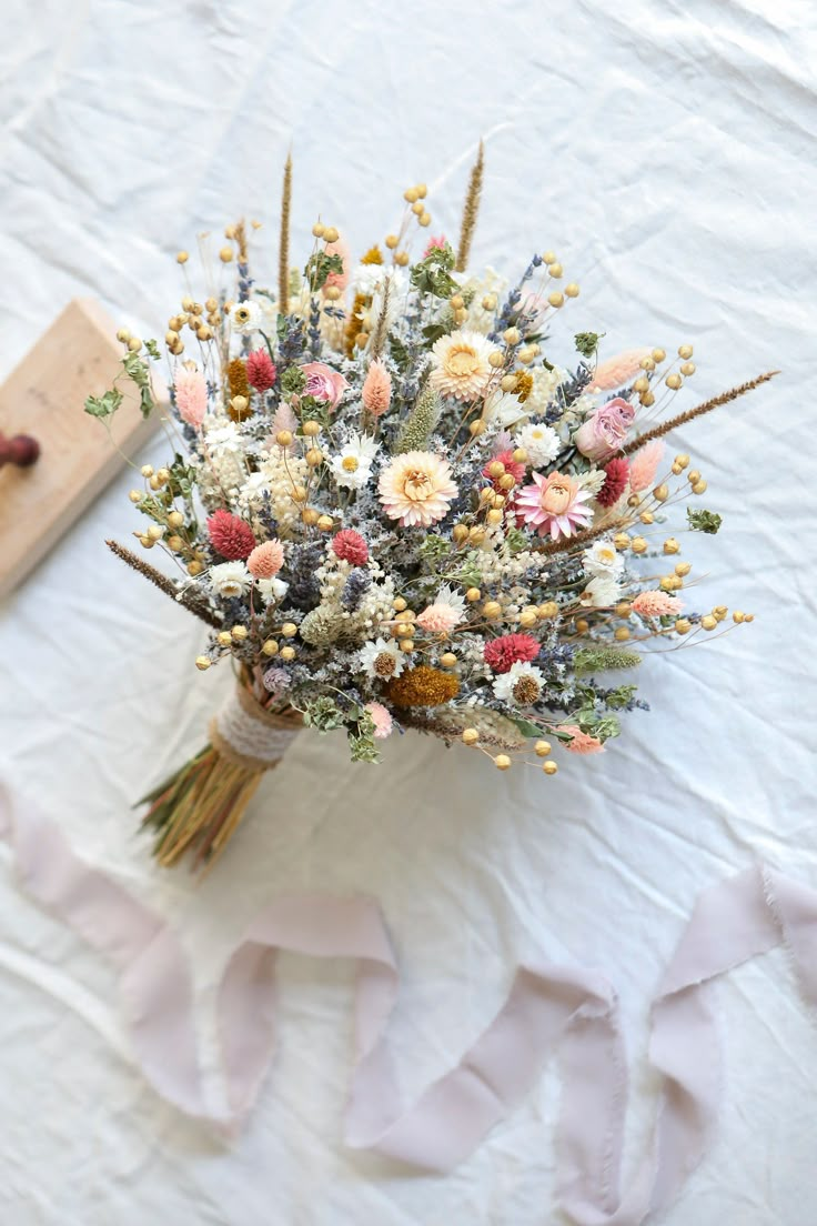 a bouquet of flowers sitting on top of a white table cloth next to a piece of wood