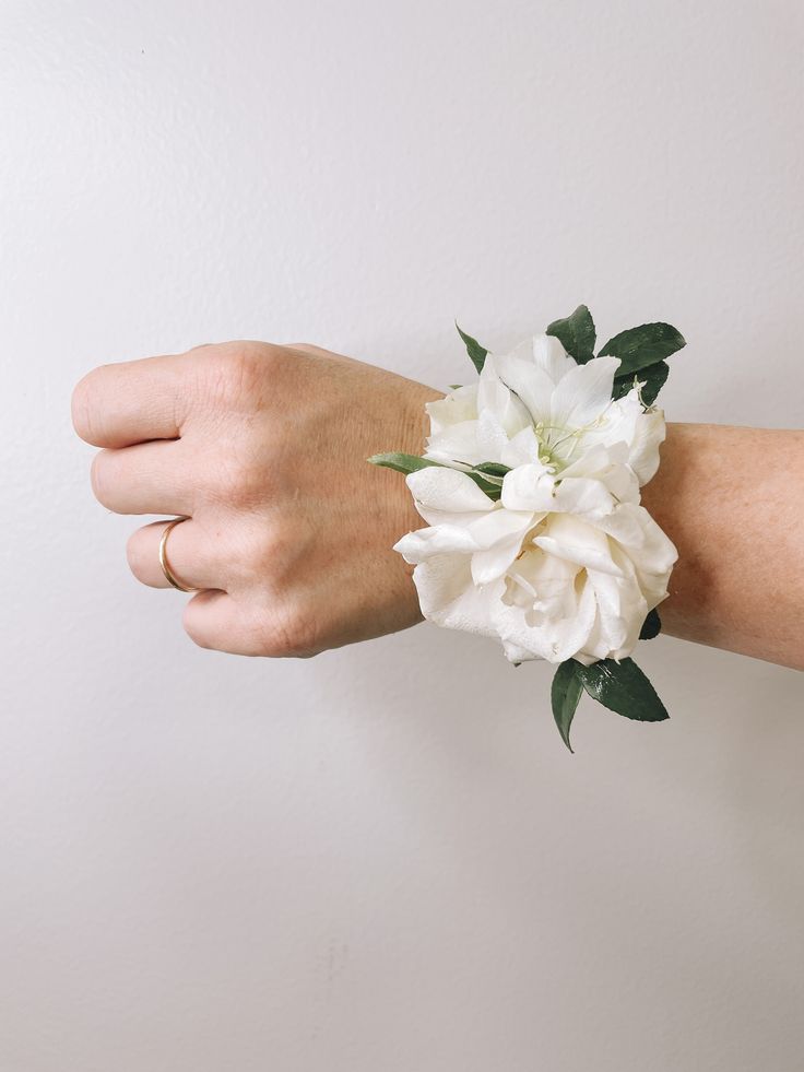 a woman's hand with a white flower on her wrist, against a white wall