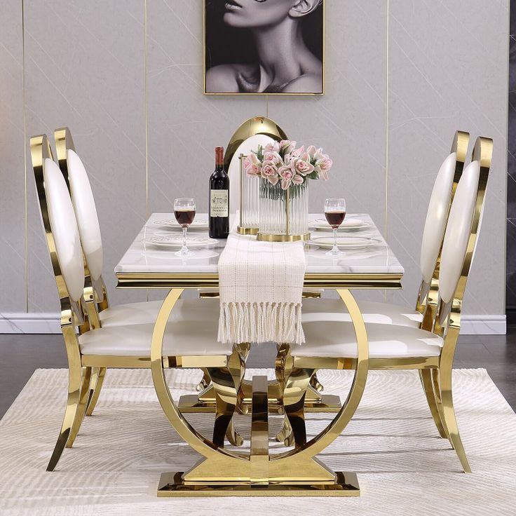 a white and gold dining room table with four chairs, two vases on each side