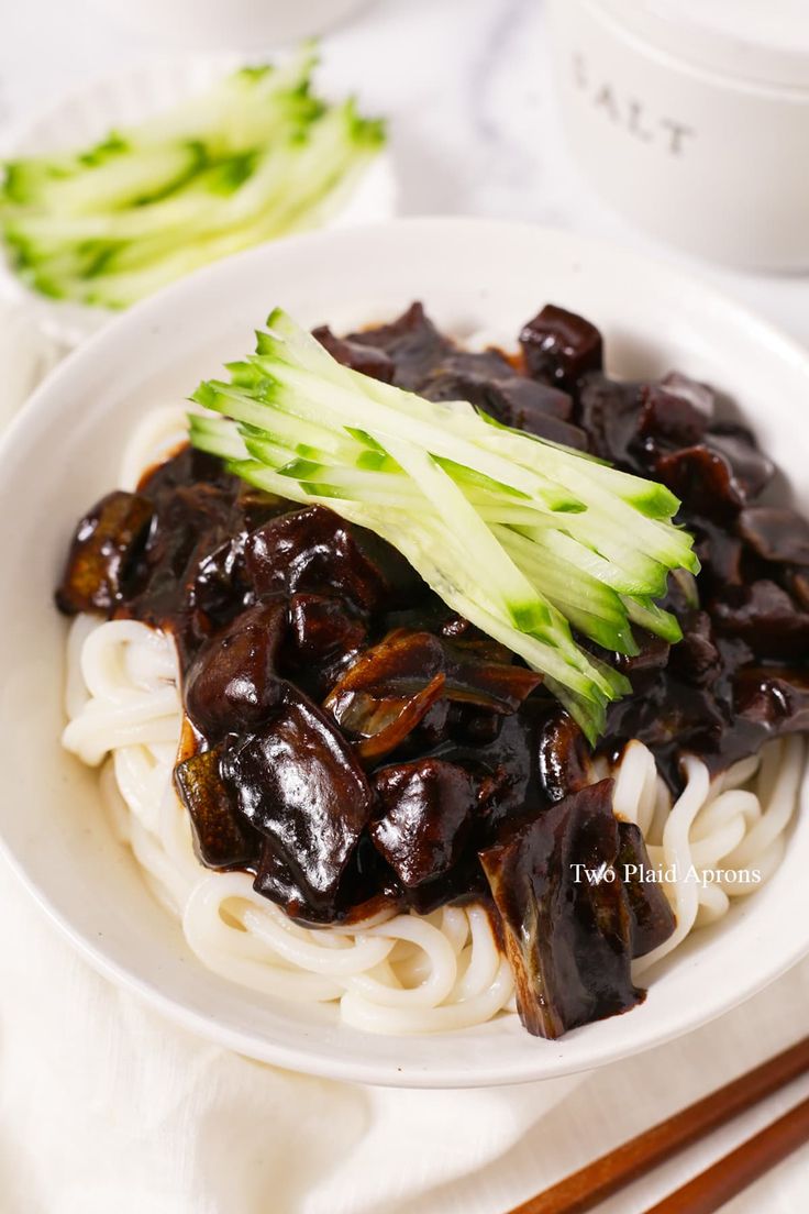 a white plate topped with noodles covered in sauce and broccoli next to chopsticks