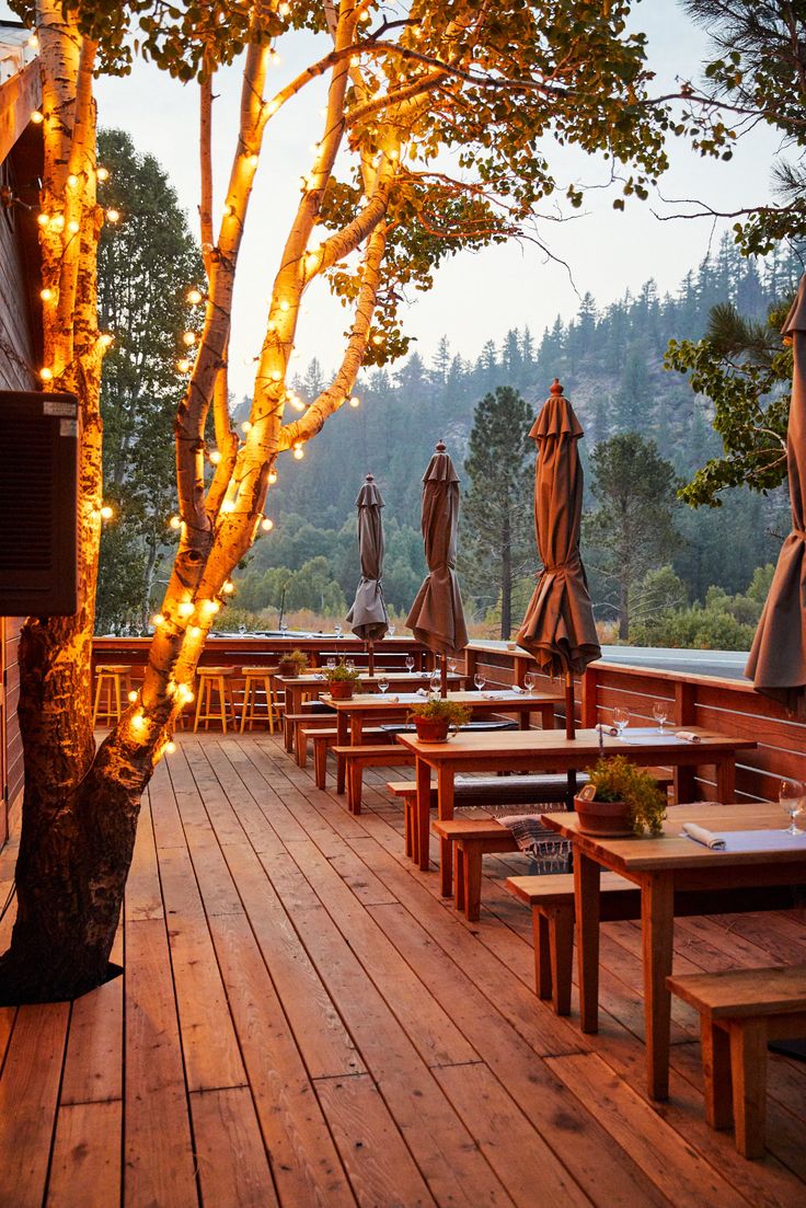 an outdoor deck with tables and umbrellas lit up by lights on the tree branches