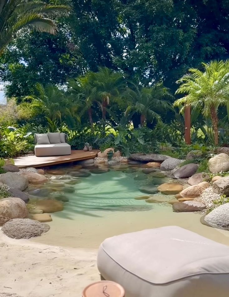 a pool surrounded by rocks and trees with a lounge chair in the middle next to it