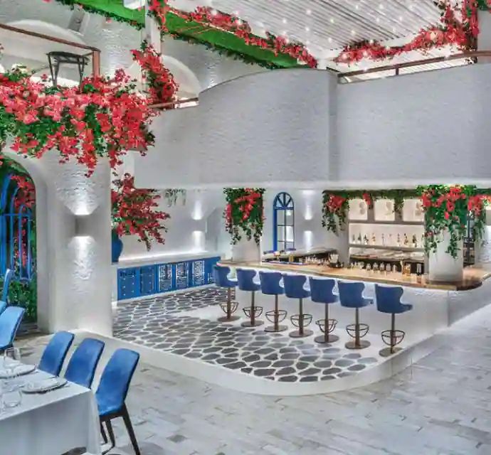 an indoor dining area with blue chairs and flowers hanging from the ceiling, along with potted plants