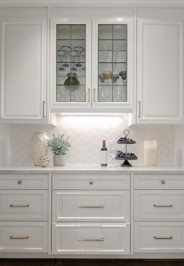 a kitchen with white cabinets and glass front cupboards on the countertop, along with an area rug