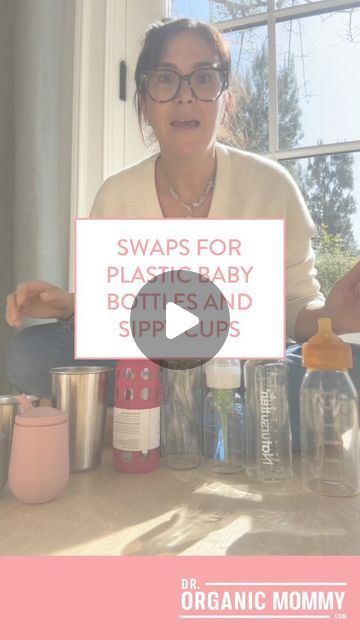 a woman sitting in front of a window holding a bottle with the words swaps for plastic baby bottles and sippy cups