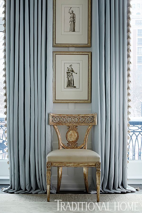 a chair sitting in front of a window covered in blue drapes and paintings on the wall