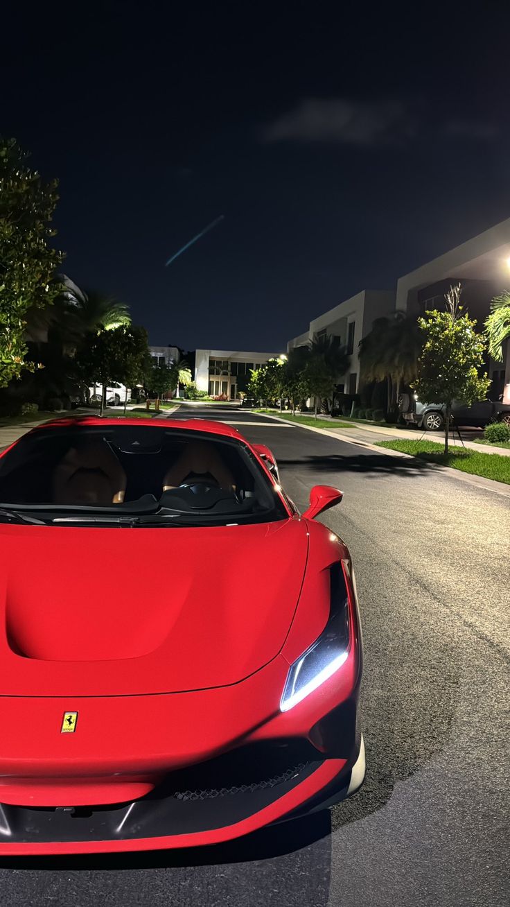 a red sports car driving down a street at night