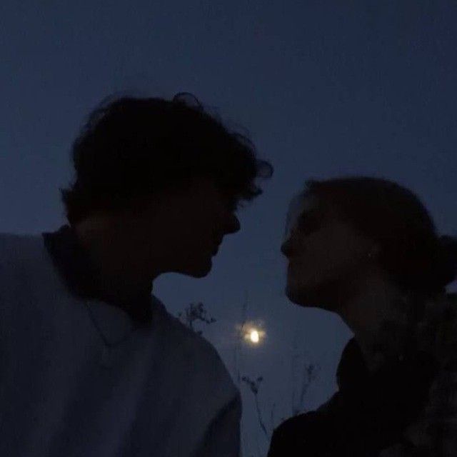 two people standing next to each other in front of a full moon at night time