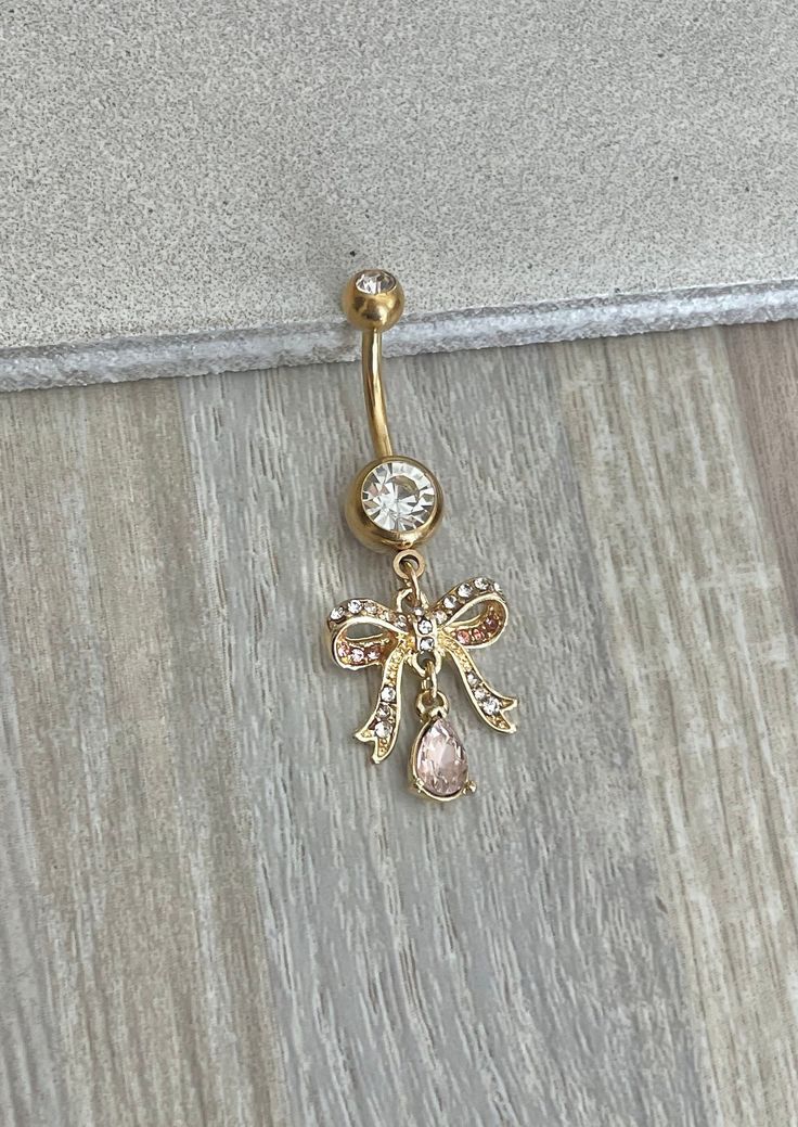 a gold colored belly ring with an angel design on the front and back, attached to a wooden floor