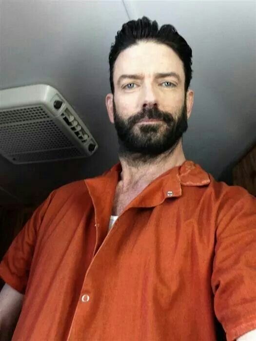 a bearded man in an orange shirt is sitting next to a wall mounted air conditioner