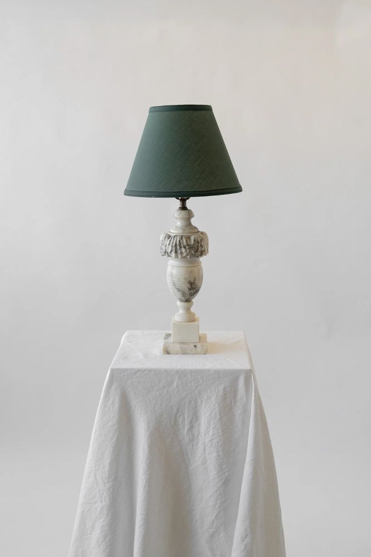 a white table with a green lamp on it and a white cloth draped around the base