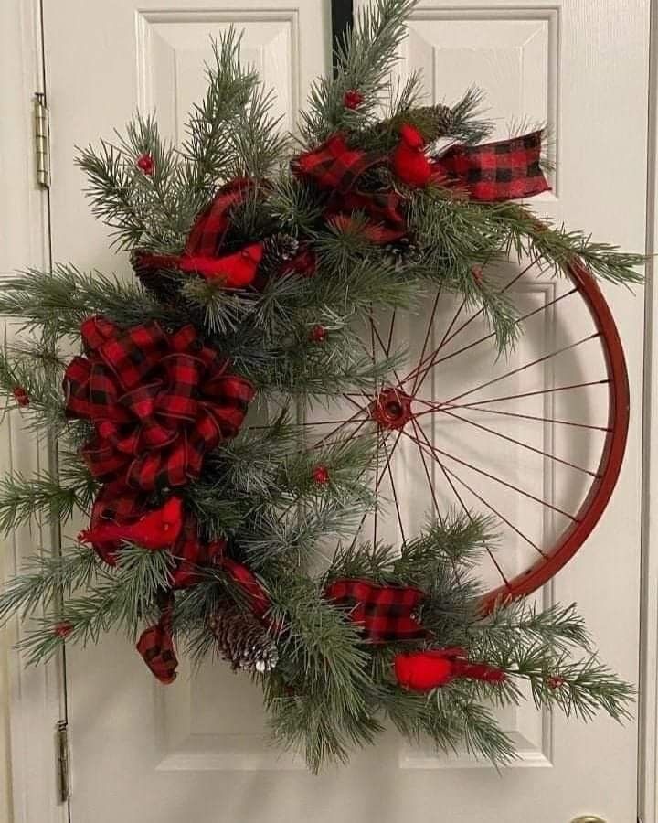 a bicycle wheel wreath with red and black plaid bows hanging on the front door for christmas