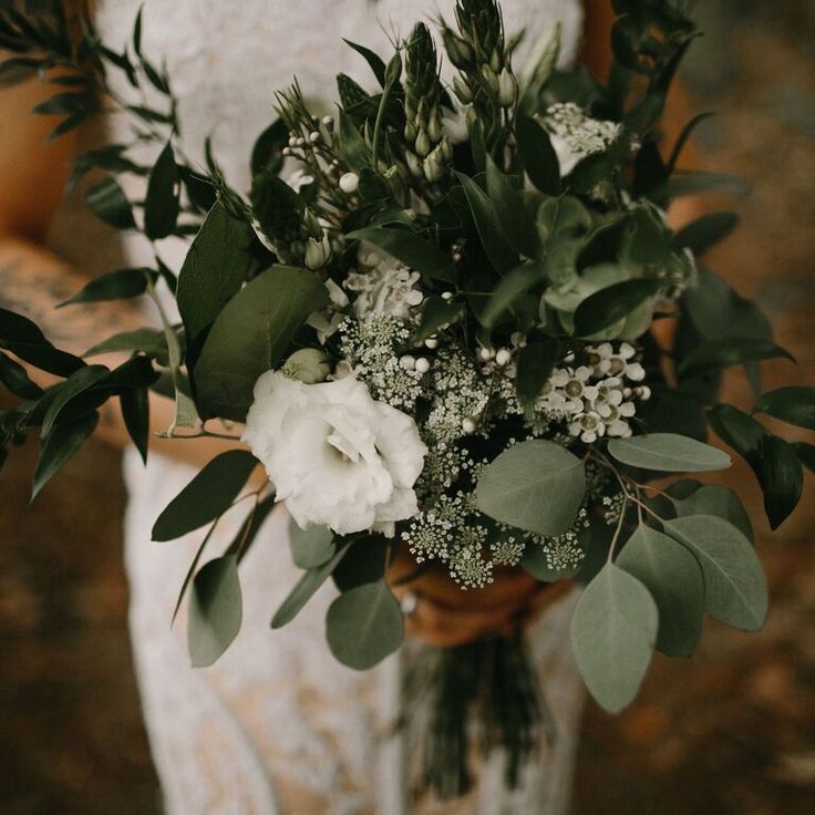 a bride holding a bouquet of flowers and greenery