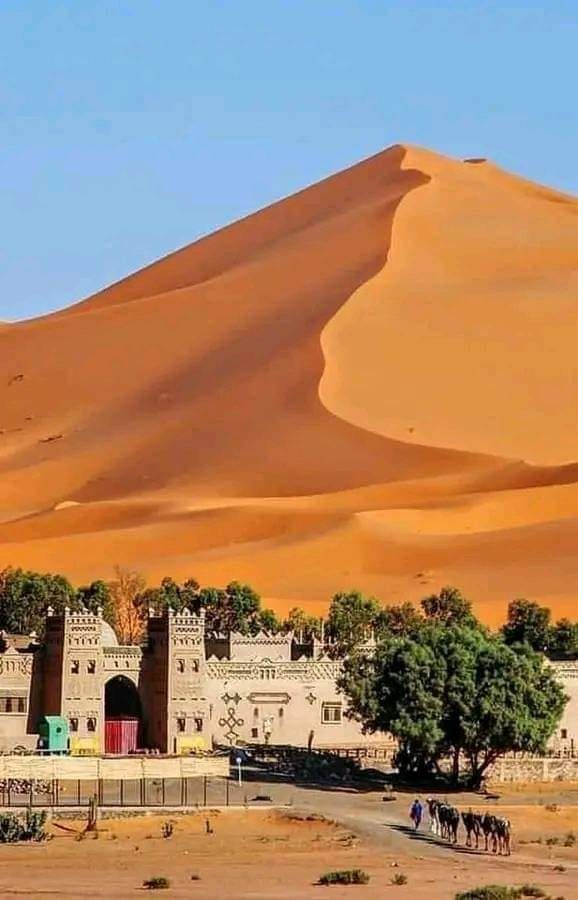 the desert is full of sand dunes and buildings, with people walking in front of them