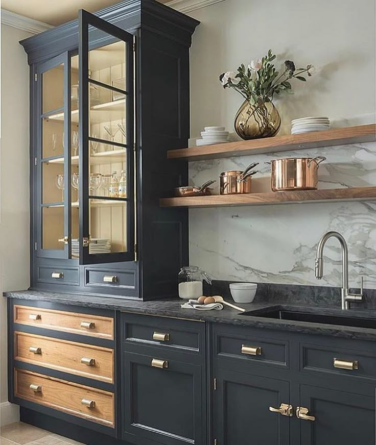 a kitchen with black cabinets and marble counter tops, gold pulls on the doors and brass knobs