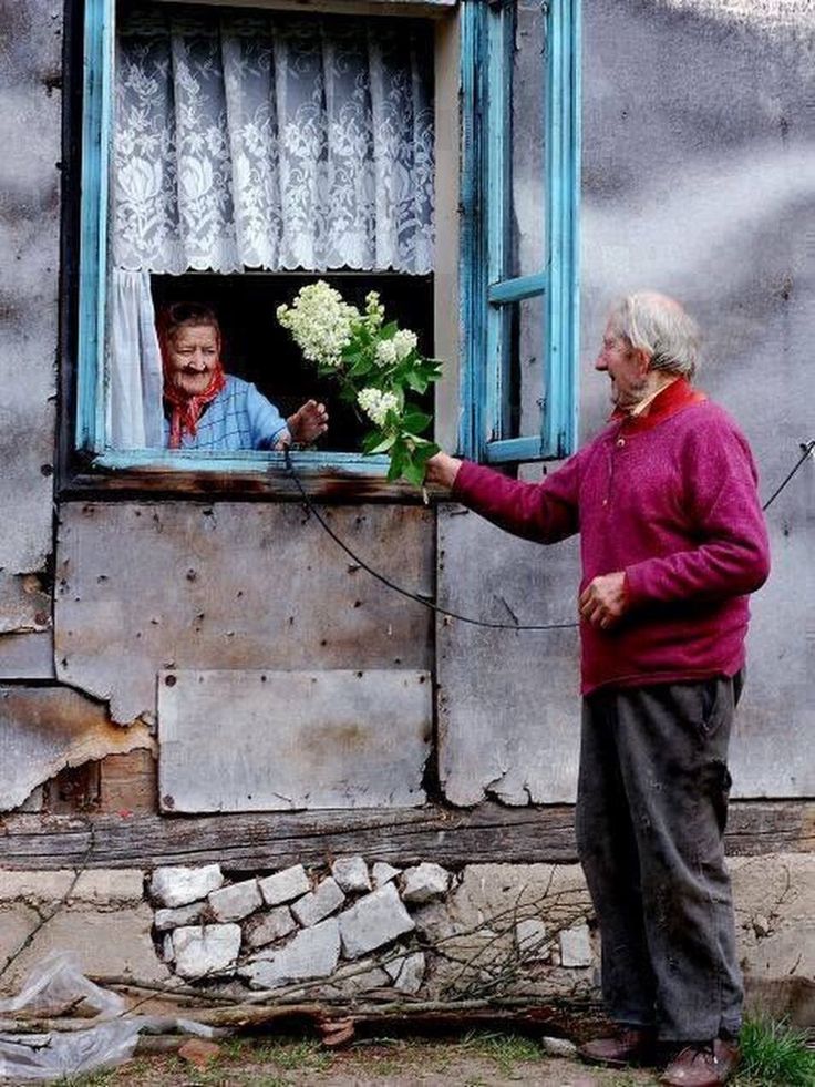 an older woman is looking out the window at another old man with flowers in his hand