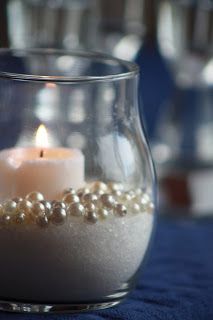 a candle that is sitting inside of a glass vase with some pearls on the side