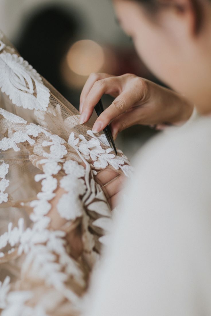 a woman in a white dress is working on her wedding dress with a pair of scissors