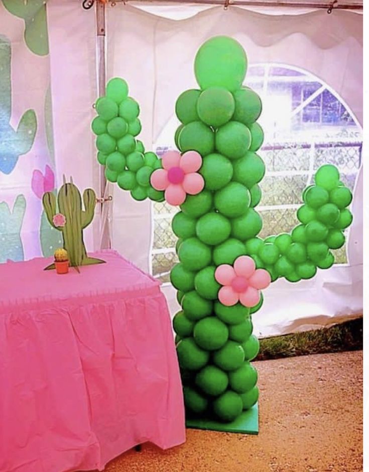 there is a large balloon cactus next to a table with a pink cloth on it