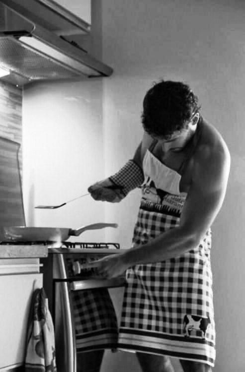 a shirtless man is cooking in the kitchen while wearing an apron and holding a spatula