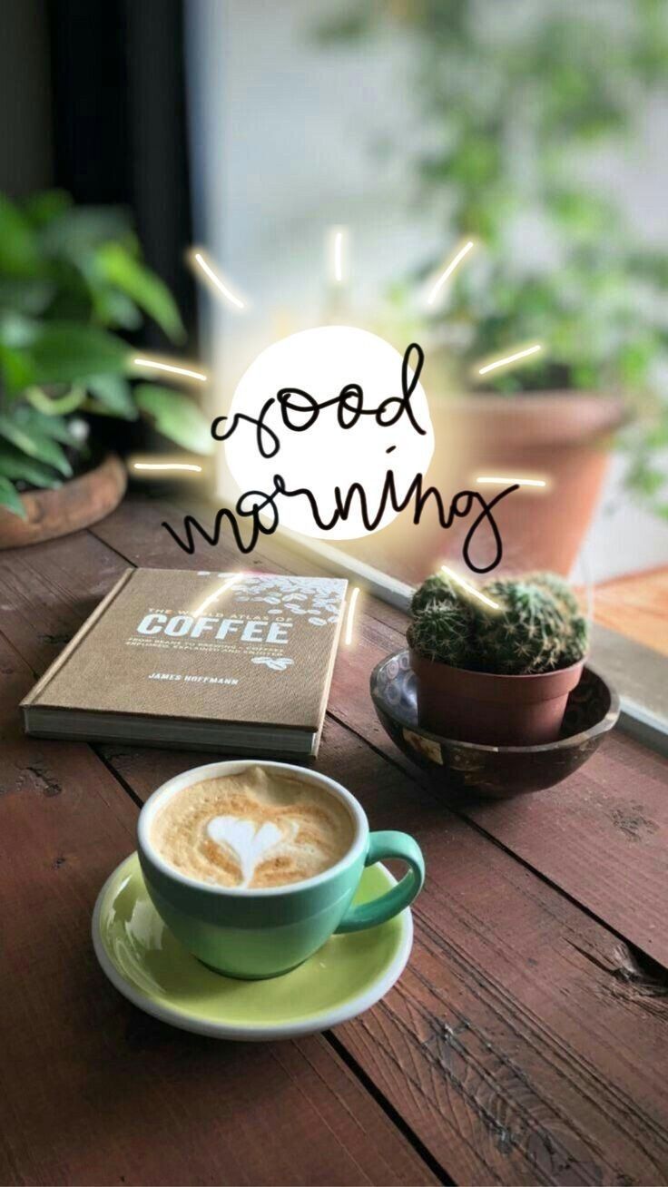 a cup of coffee sitting on top of a wooden table next to a book and potted plant