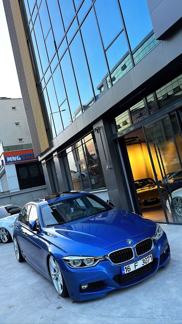 two blue cars parked in front of a building with glass windows on the side of it