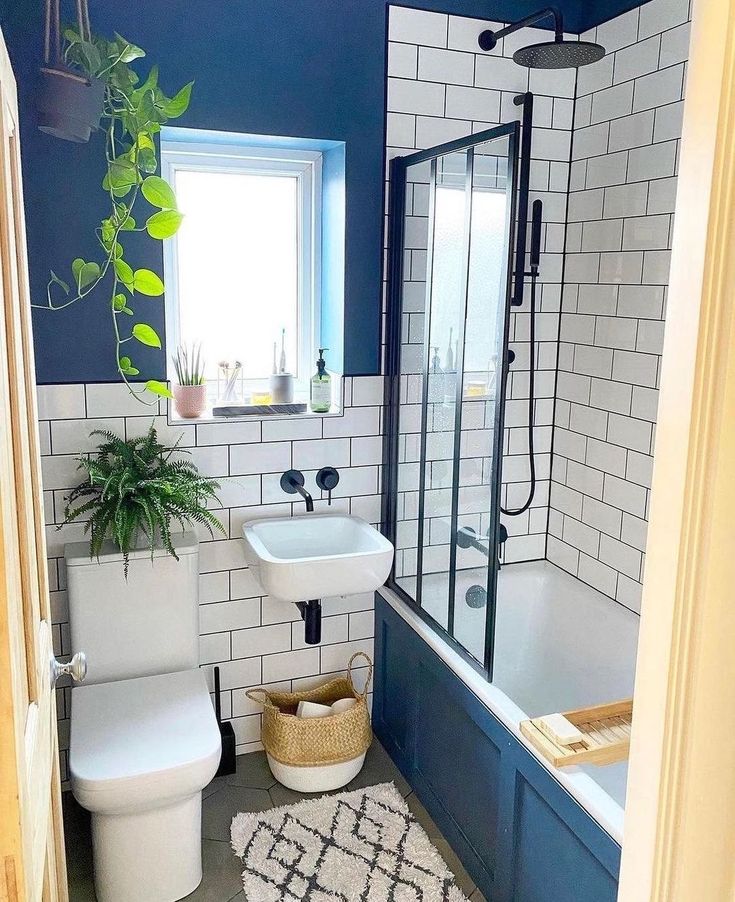 a white toilet sitting next to a bath tub in a bathroom under a window with a potted plant