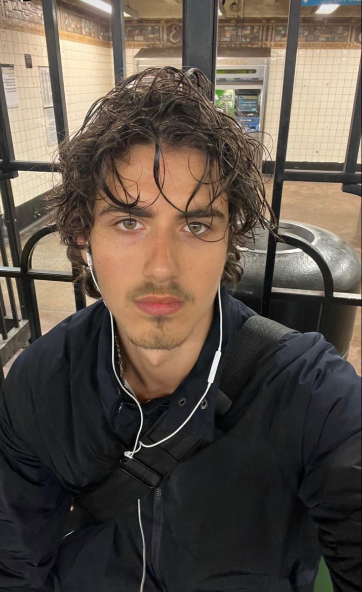 a man with headphones on sitting in front of a train station platform and looking at the camera