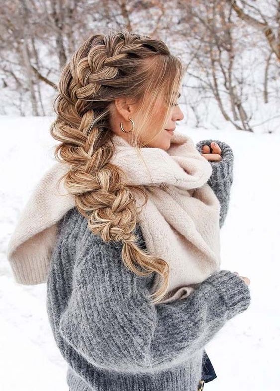 a woman standing in the snow with her hair in a fishtail braid and wearing a sweater