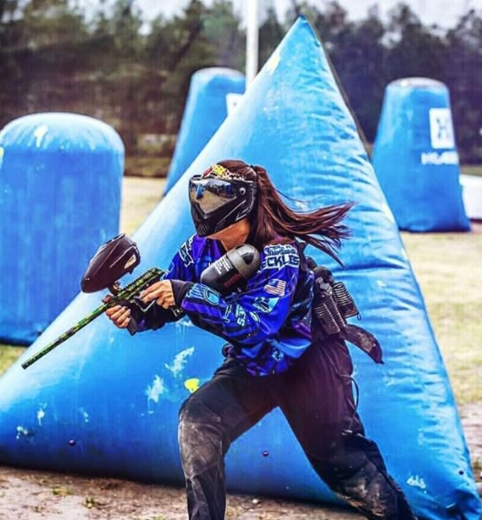 a woman is playing paintball in an obstacle course