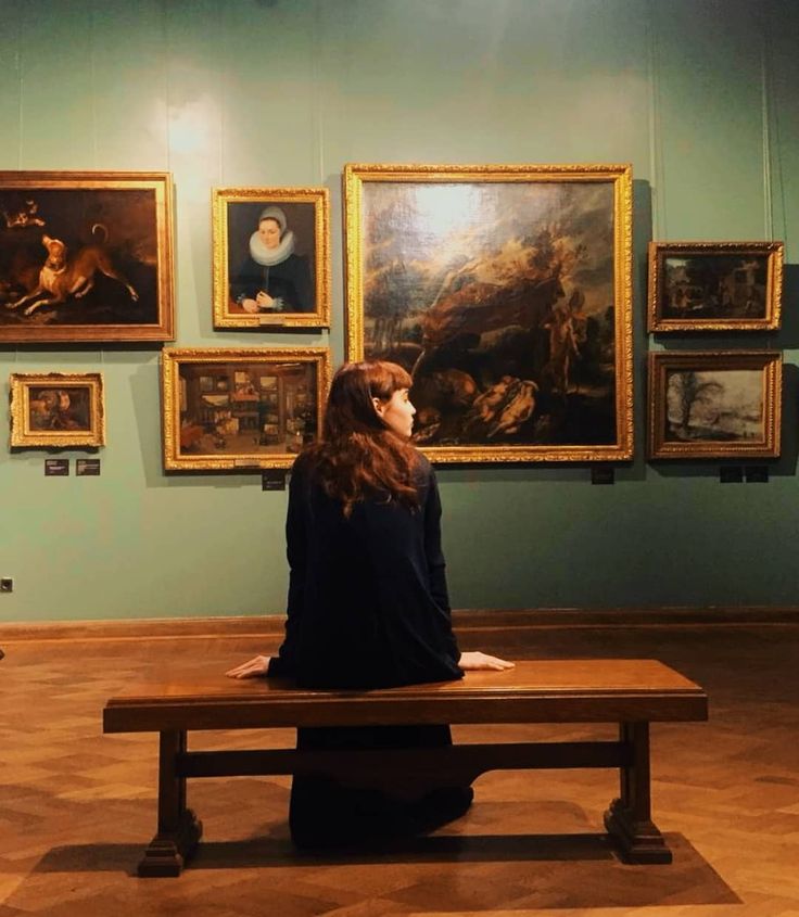 a woman sitting on a bench in front of some paintings and looking at the sky