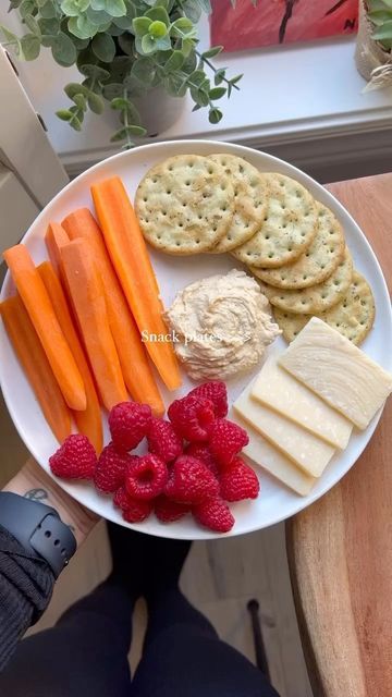 a white plate topped with crackers, carrots and crackers next to raspberries