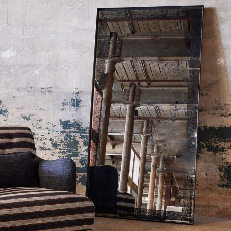 a chair sitting in front of a large mirror on top of a wooden floor next to a wall