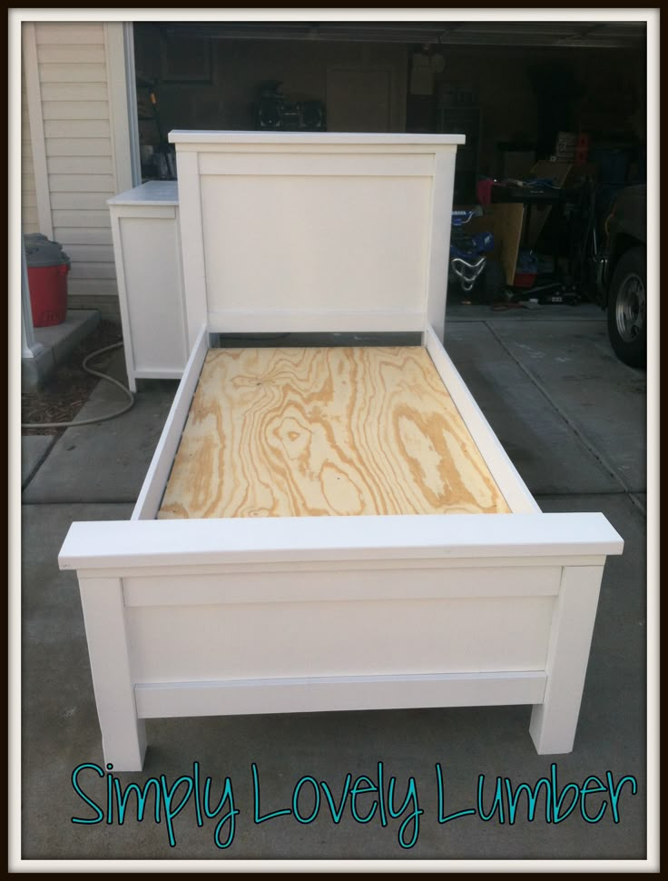 a white bed frame with wood slats on the top and bottom, in front of a garage