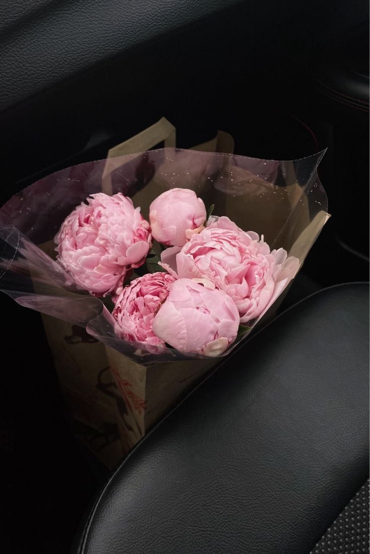 a bunch of pink flowers sitting inside of a bag on the back seat of a car