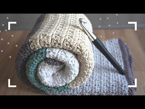 a crocheted blanket folded on top of a wooden floor with an open crochet hook