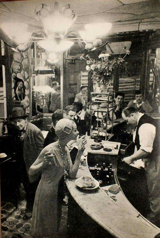 an old black and white photo of people in a room with many items on the table