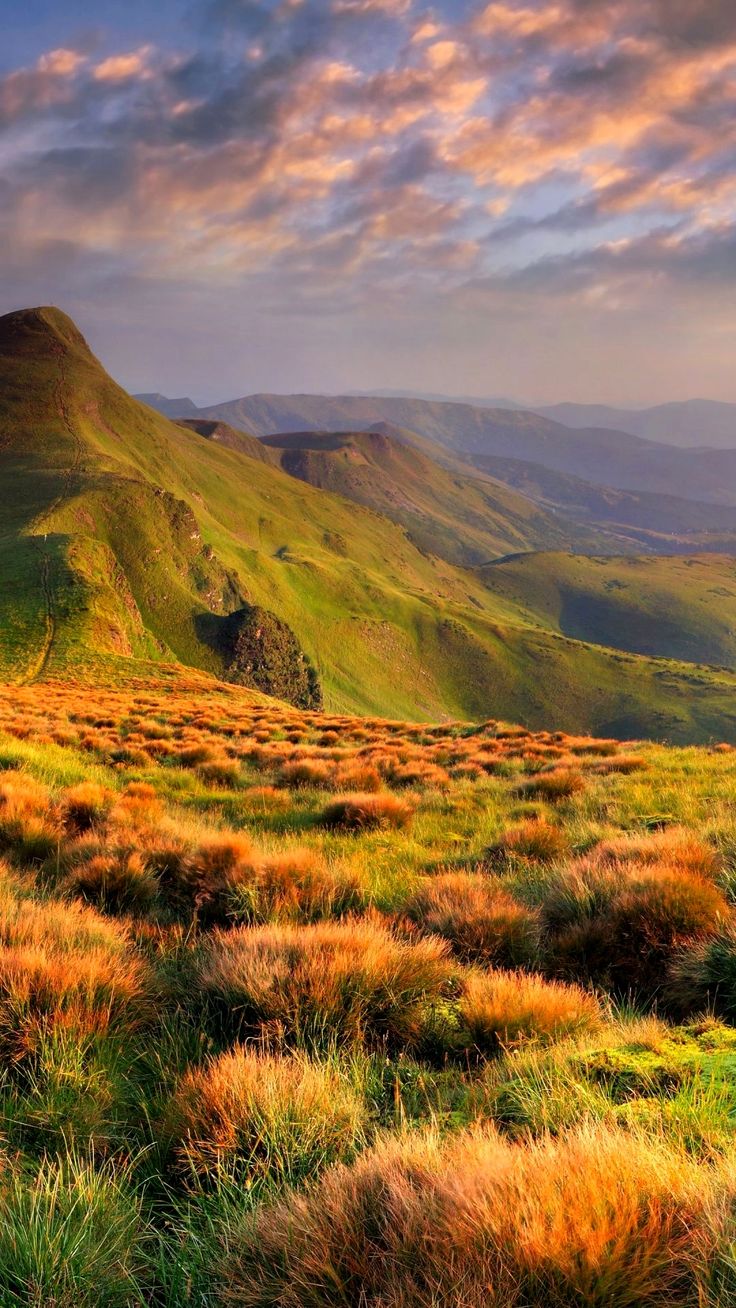 the mountains are covered in green grass and brown grasses, as well as some clouds