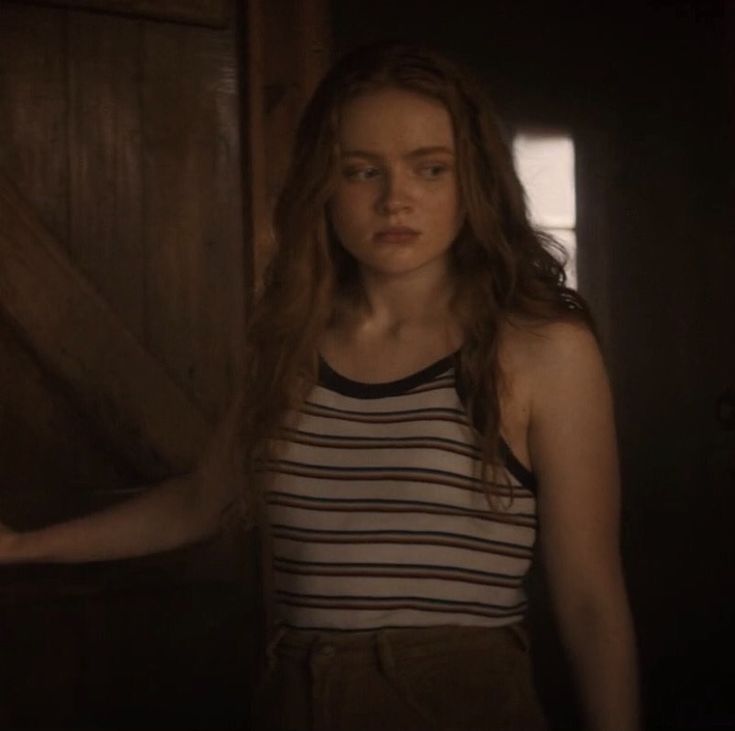 a woman with long hair standing in front of a wooden door and looking at the camera