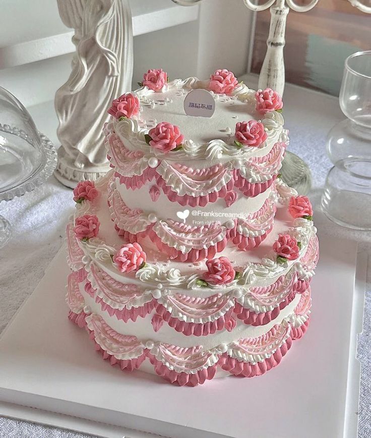 a wedding cake is decorated with pink flowers and ribbons on a white tableclothed place mat