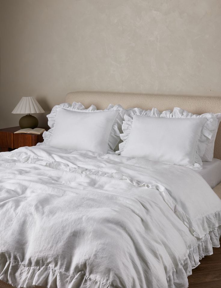 the bed is made with white linens and ruffles on it's headboard