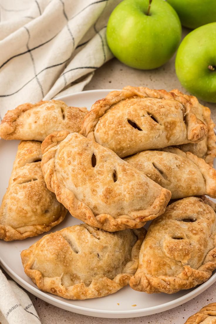 a white plate topped with apple pies next to green apples