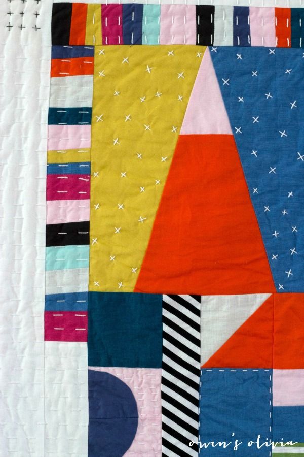 a quilted wall hanging on the side of a white wall with an orange, blue, and pink patchwork design