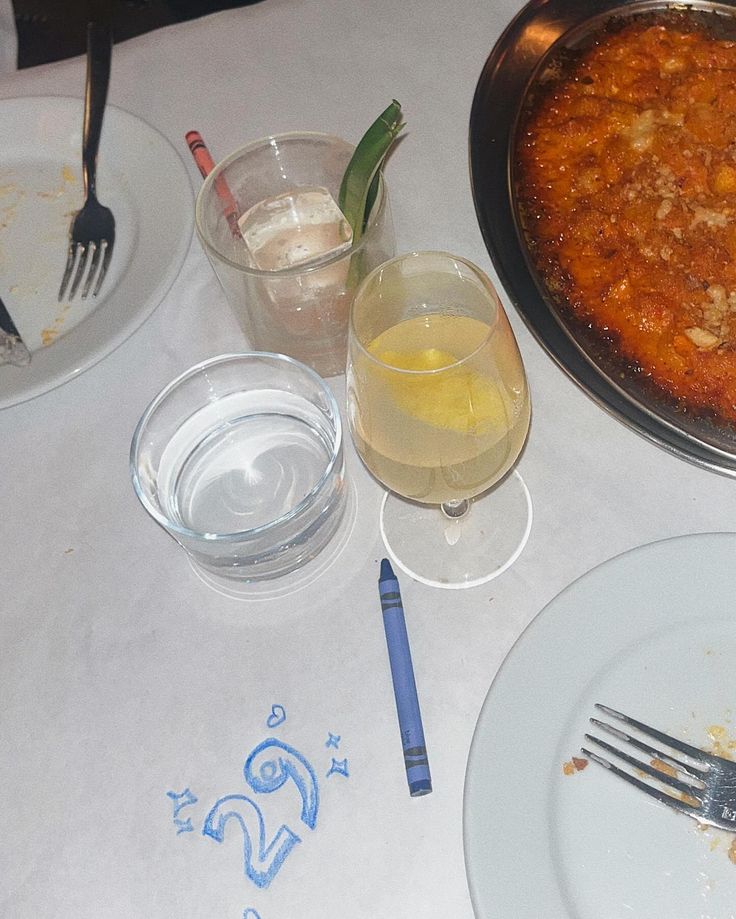 a table topped with plates and silverware next to a pan filled with food on top of a white table cloth