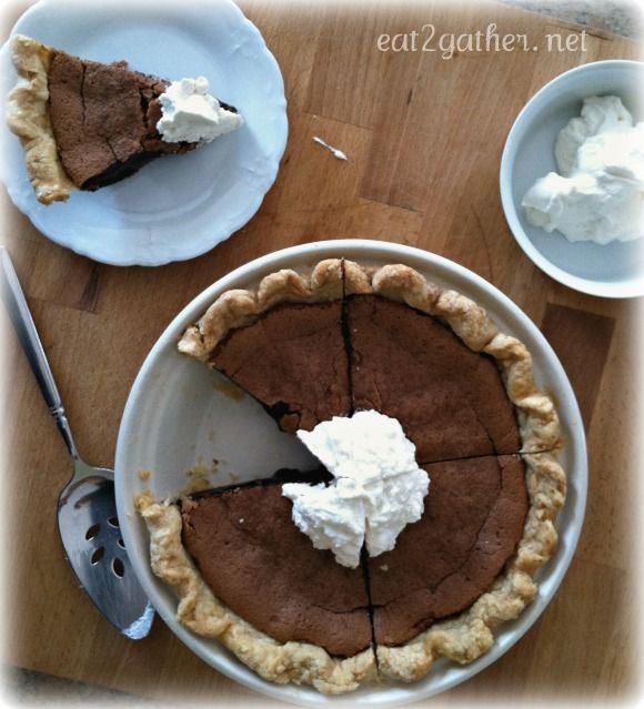 there is a chocolate pie on the table with whipped cream and spoons next to it