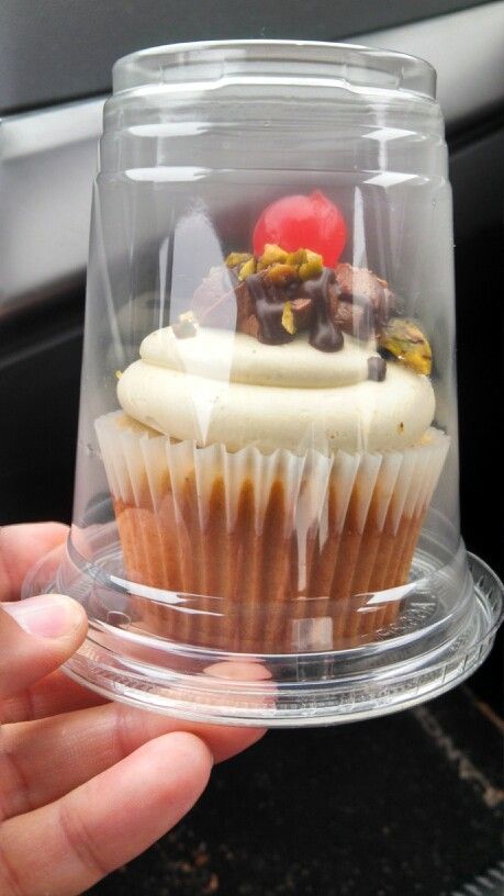 a cupcake with white frosting and toppings in a clear plastic container on top of a car dashboard