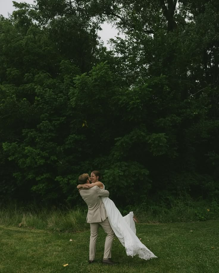 a bride and groom hug in the middle of their wedding day, surrounded by trees