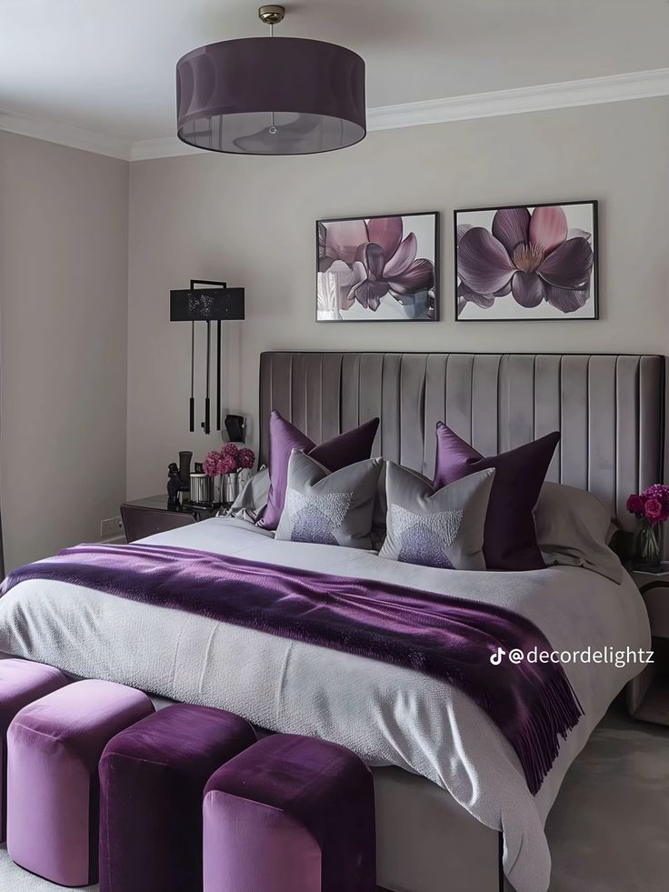 a large bed with purple pillows and matching foot stools in a room that has two pictures on the wall above it